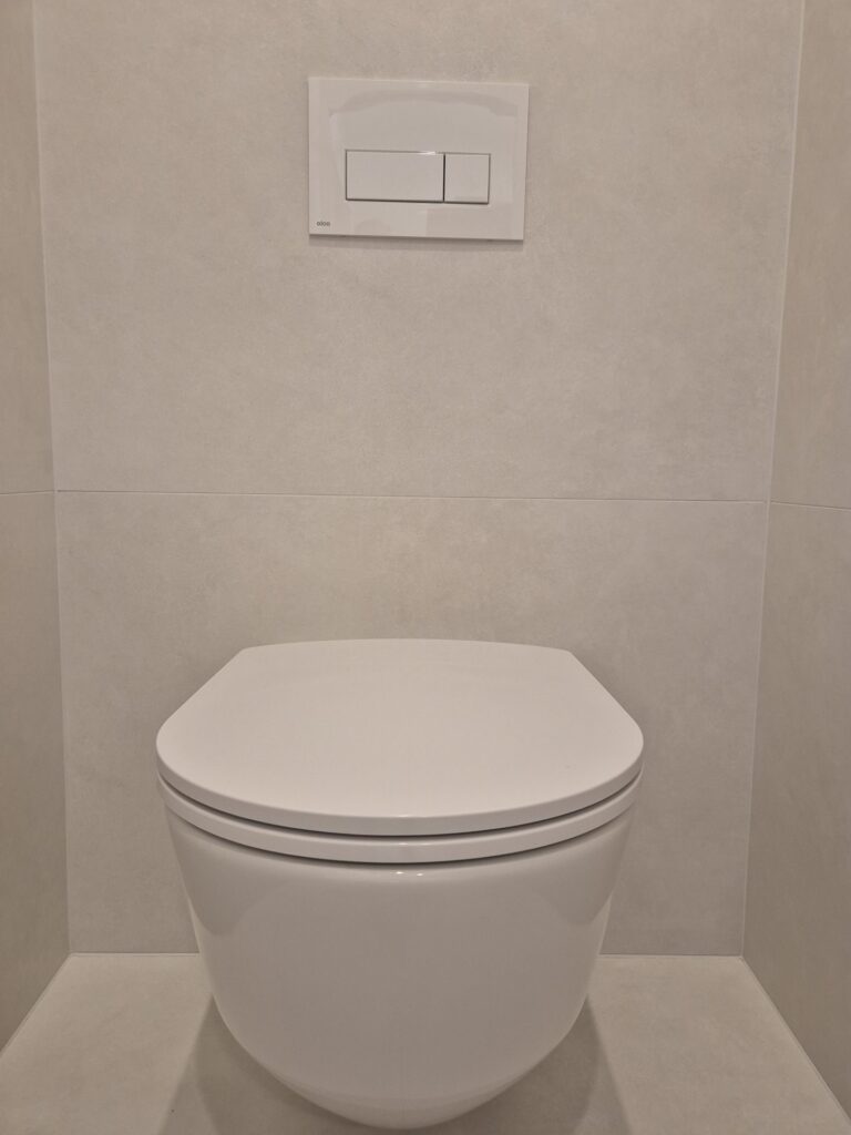 Závěsné WC s bílým ovládacím tlačítkem a béžovým obkladem, Praha Prosek